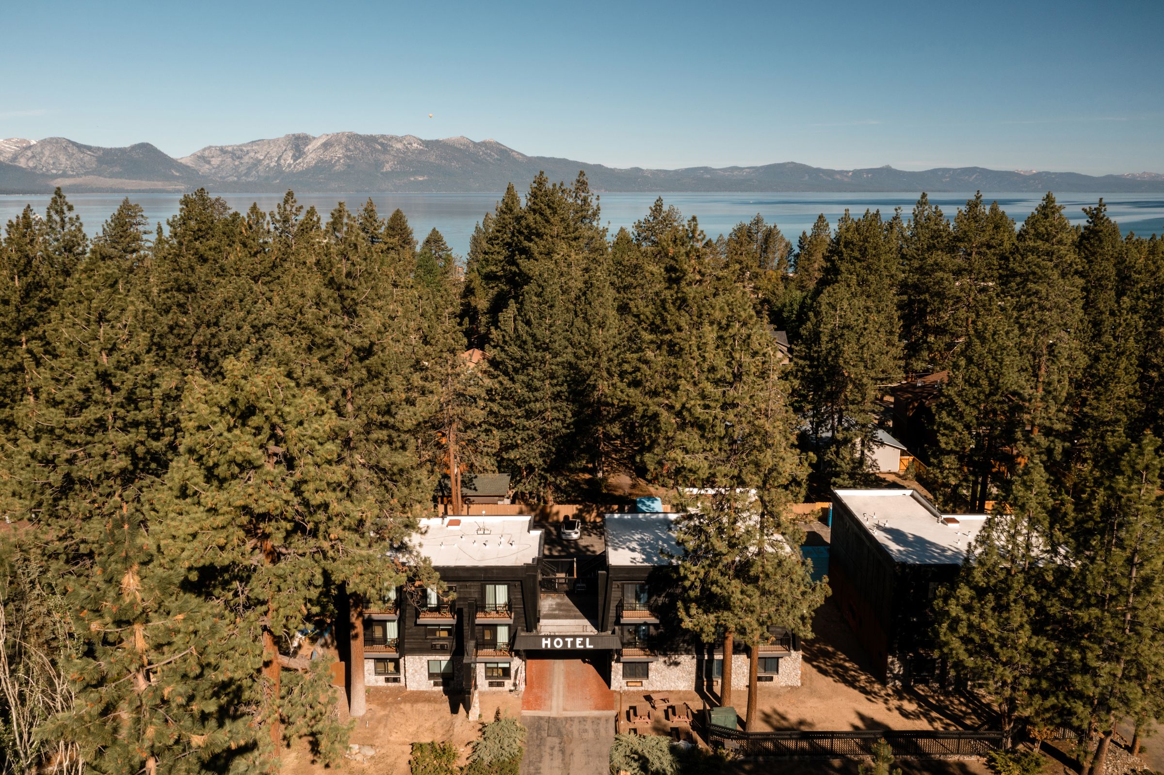 Aerial view of The Coachman among pine trees, with Lake Tahoe and the mountains behind