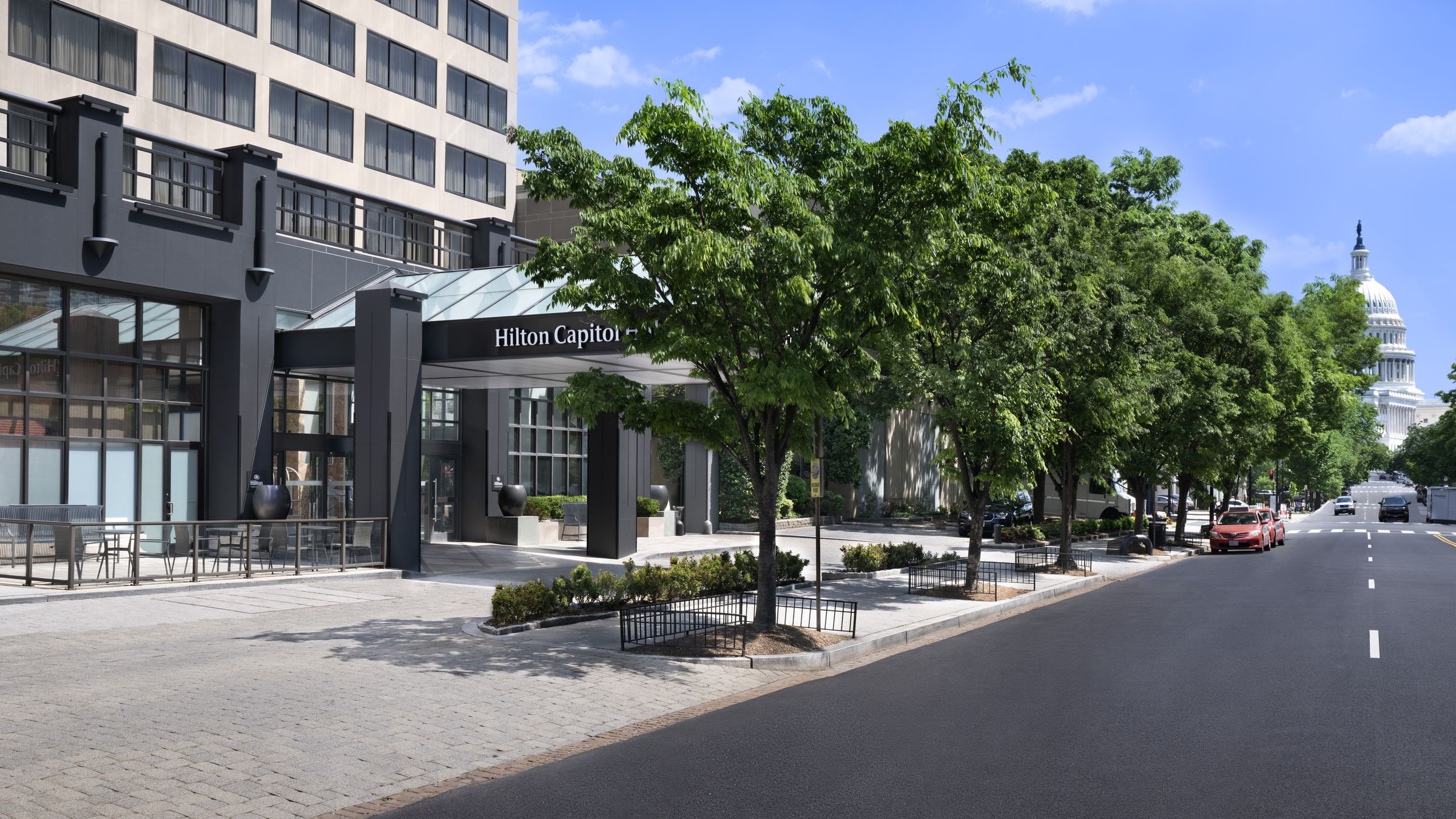 Hilton Capitol Hill on a tree-lined street, with the U.S. Capitol dome beyond